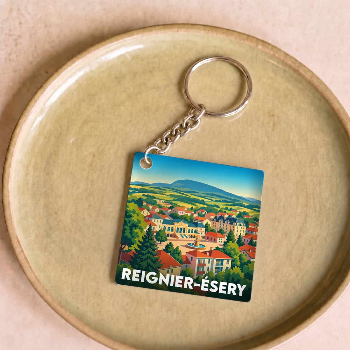 Porte-clés souvenir de la ville de Reignier-Ésery avec une illustration colorée et stylisée du paysage local.