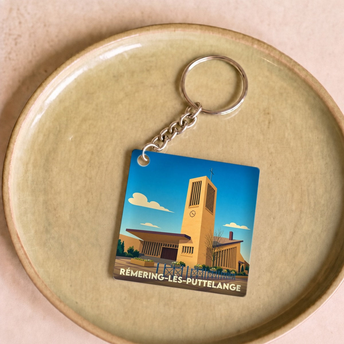 Porte-clés souvenir de la ville de Rémering-lès-Puttelange avec une illustration stylisée de son église.