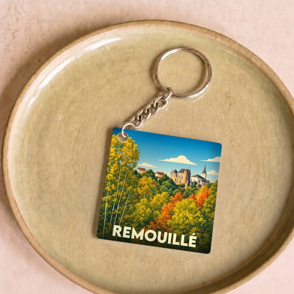 Porte-clés souvenir de la ville de Remouillé avec une illustration stylisée d'un paysage d'automne.
