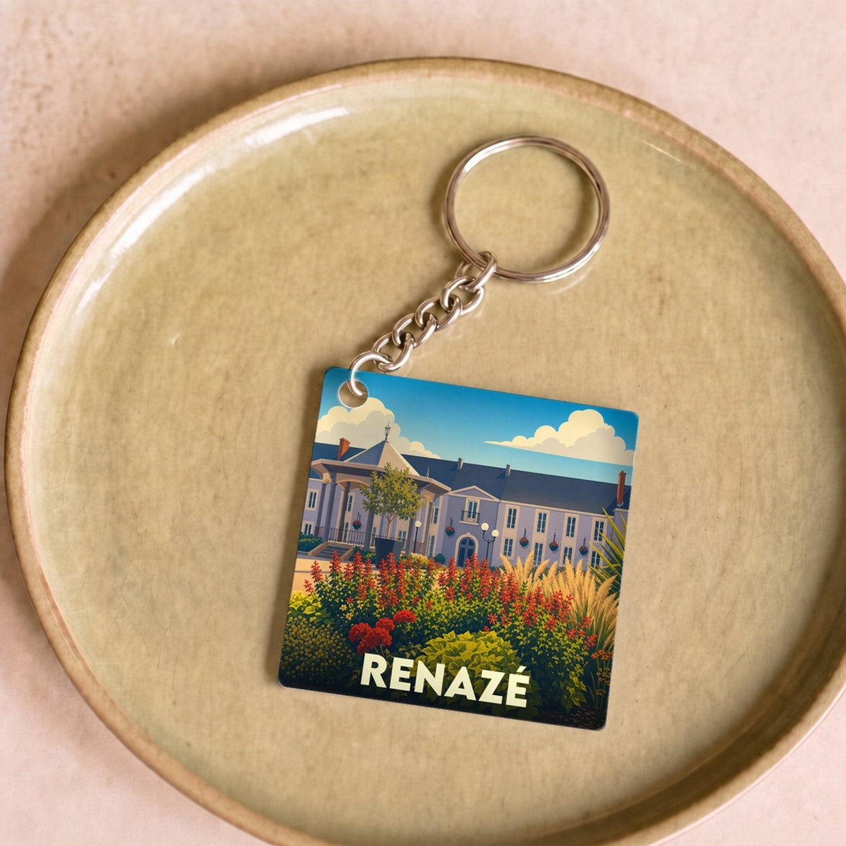 Porte-clés souvenir de la ville de Renazé avec une illustration stylisée d'un bâtiment fleuri.