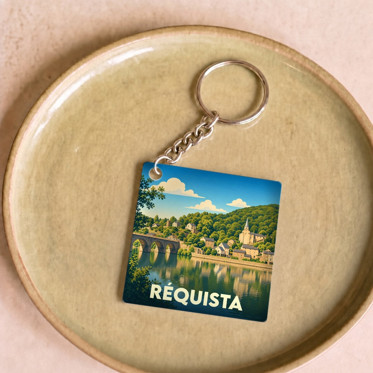 Porte-clés souvenir de la ville de Réquista avec une illustration stylisée d'un paysage fluvial.