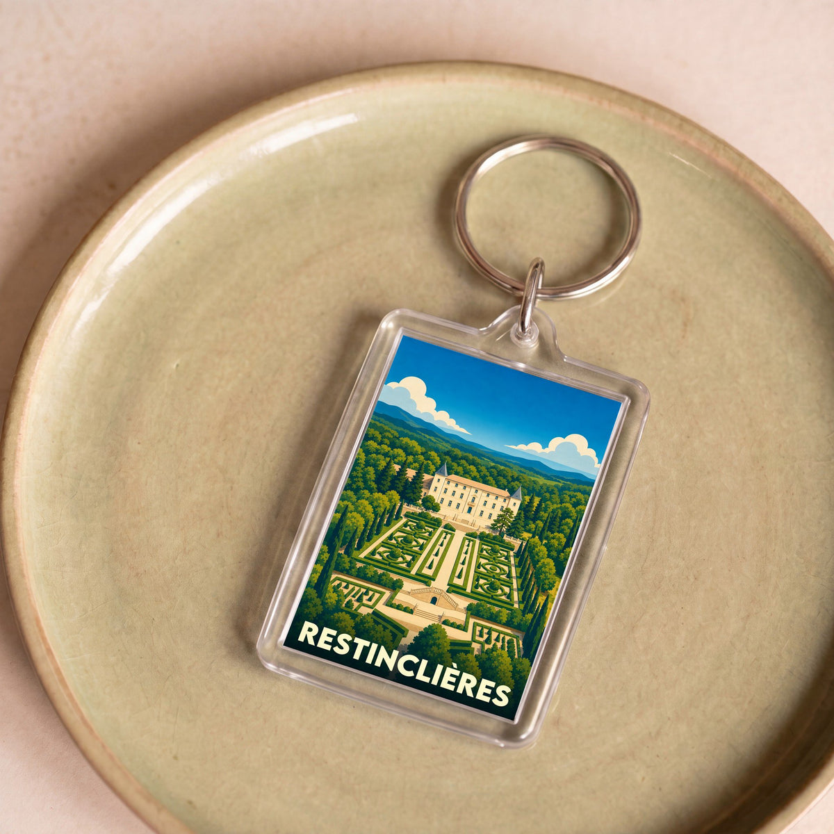 Porte-clés souvenir de Restinclières avec une illustration stylisée du château et de ses jardins.