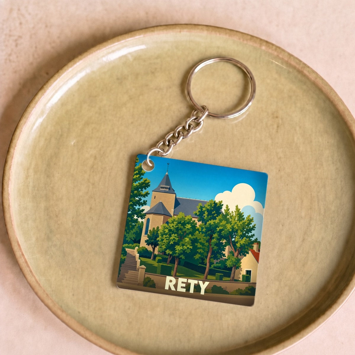 Porte-clés souvenir de la ville de Rety avec une illustration stylisée de son église entourée de verdure.
