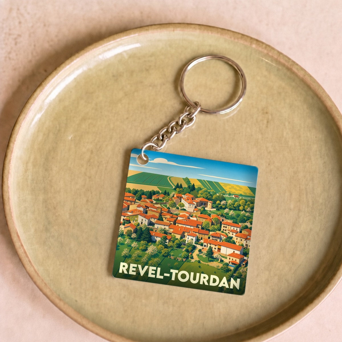 Porte-clés souvenir de la ville de Revel-Tourdan avec une illustration stylisée de ses paysages et toitures.