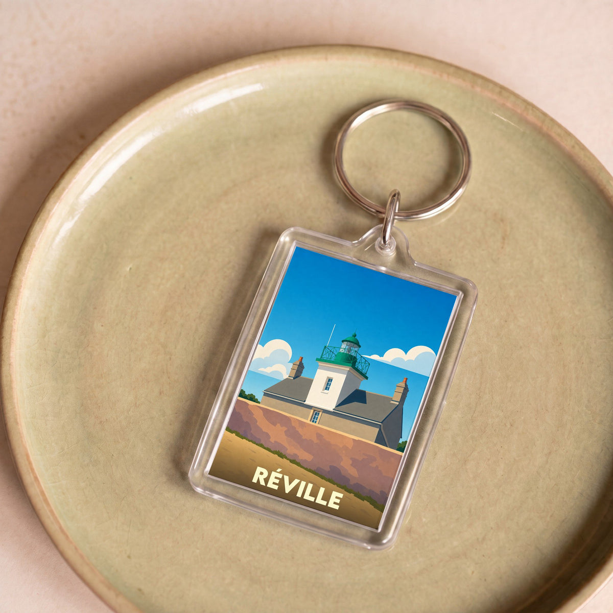 Porte-clés souvenir de la ville de Réville illustré par un phare stylisé sous un ciel bleu.