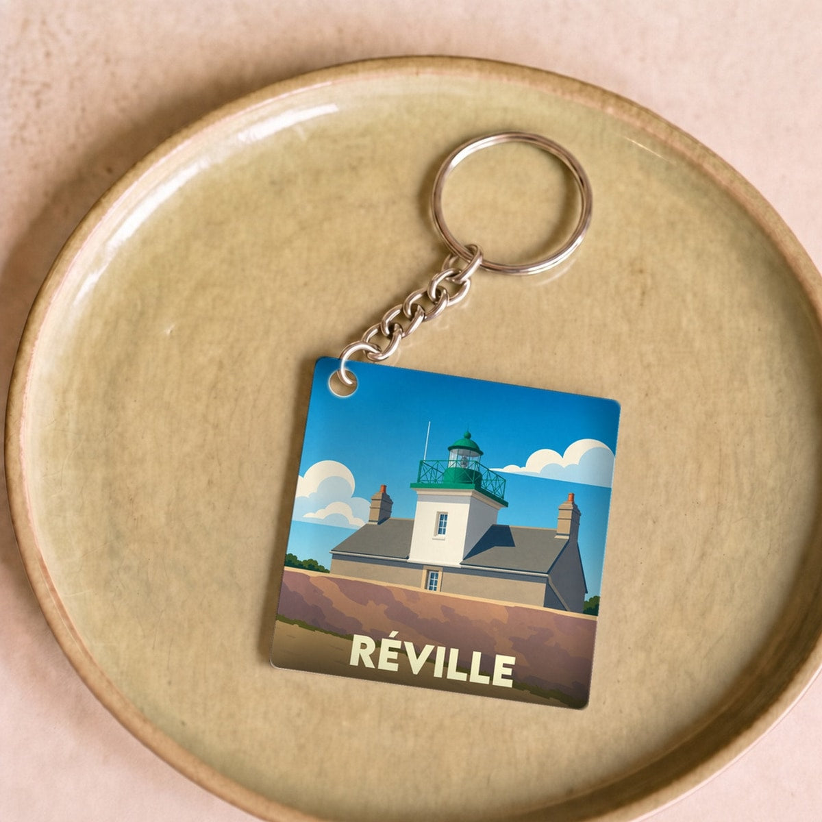 Porte-clés souvenir de la ville de Réville illustré par un phare stylisé sous un ciel bleu.