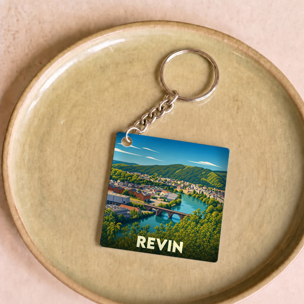 Porte-clés souvenir de la ville de Revin avec une illustration stylisée d'un paysage fluvial.