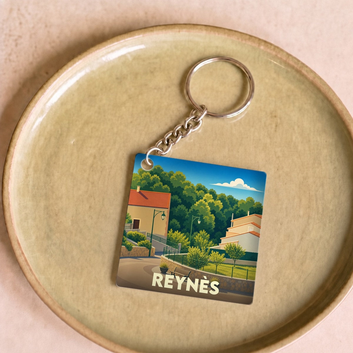 Porte-clés souvenir de la ville de Reynès avec une illustration stylisée.