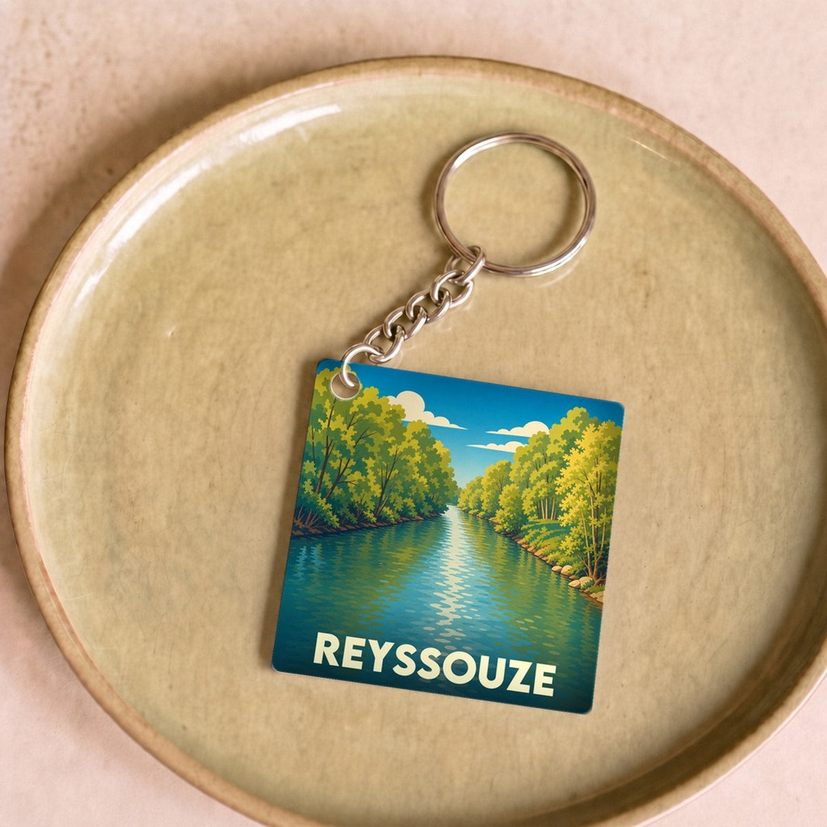 Porte-clés souvenir de la ville de Reyssouze avec une illustration stylisée d'une rivière bordée d'arbres.