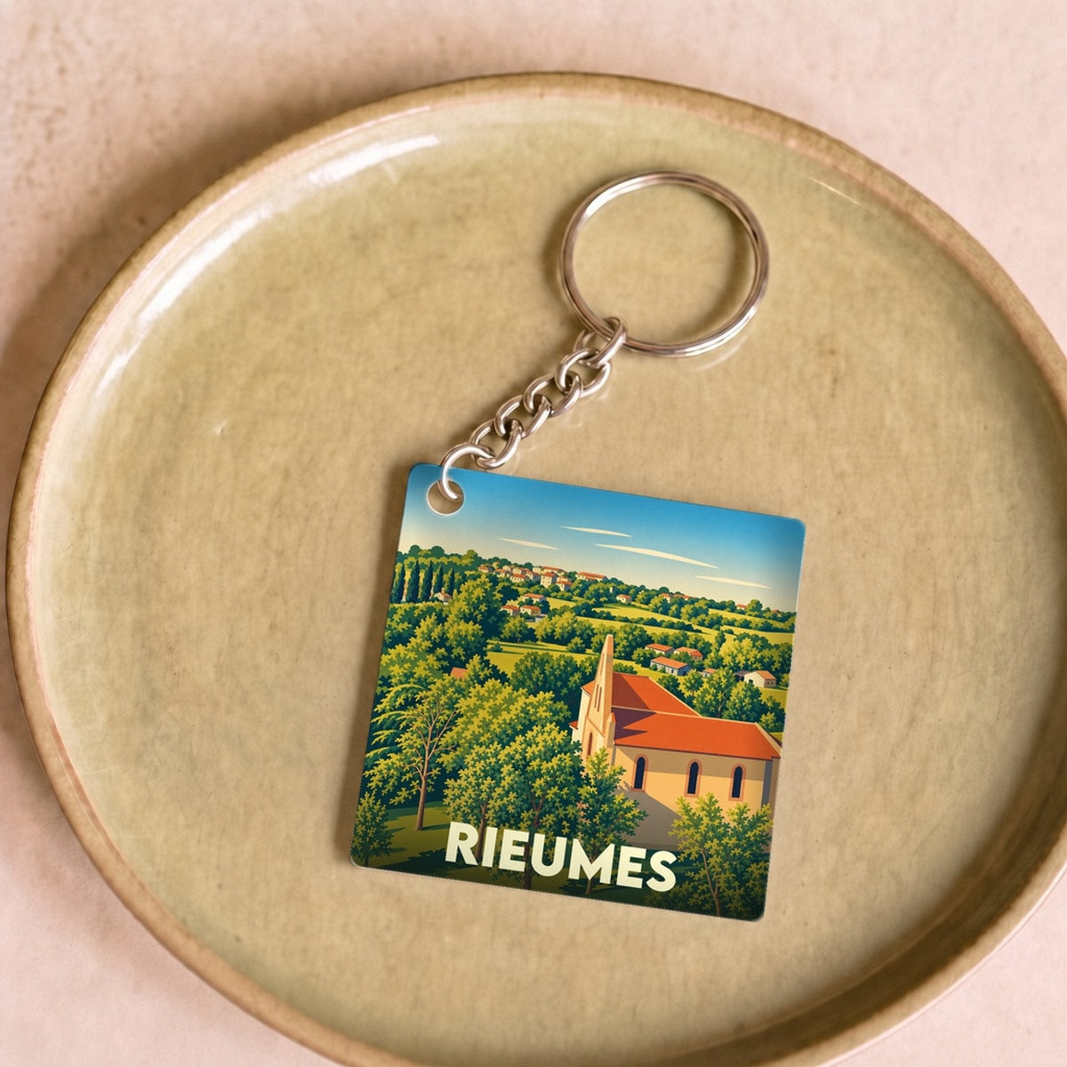 Porte-clés souvenir de la ville de Rieumes avec une illustration stylisée d'un paysage de campagne et de son église.
