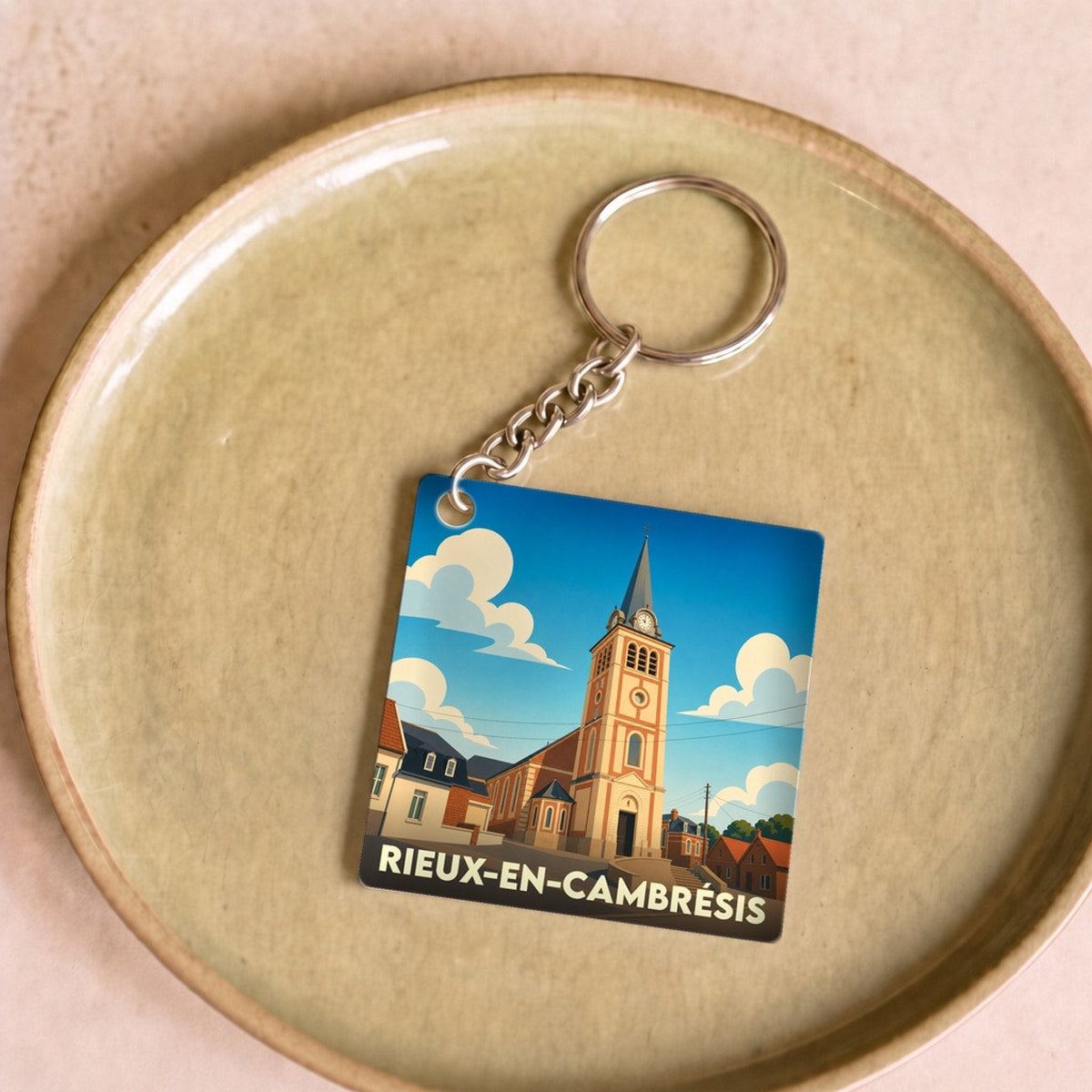 Porte-clés souvenir de la ville de Rieux-en-Cambrésis avec une illustration stylisée de son église sous un ciel bleu.