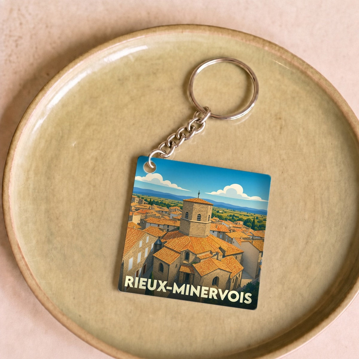 Porte-clés souvenir de la ville de Rieux-Minervois avec une illustration stylisée de son église et de ses toits.