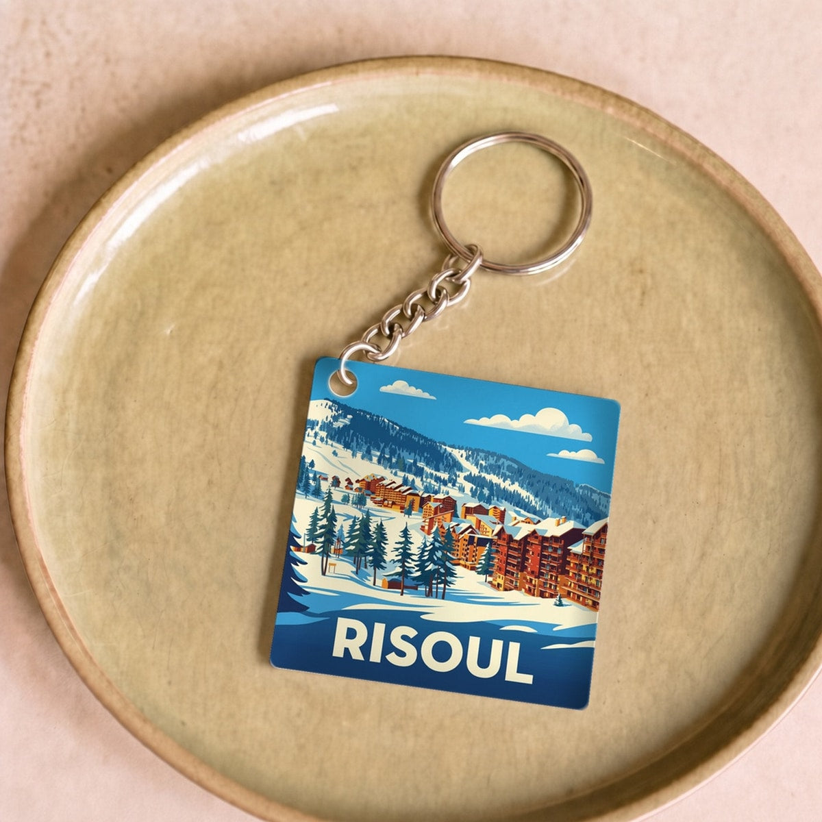 Porte-clés souvenir de la ville de Risoul avec une illustration stylisée de paysages enneigés.