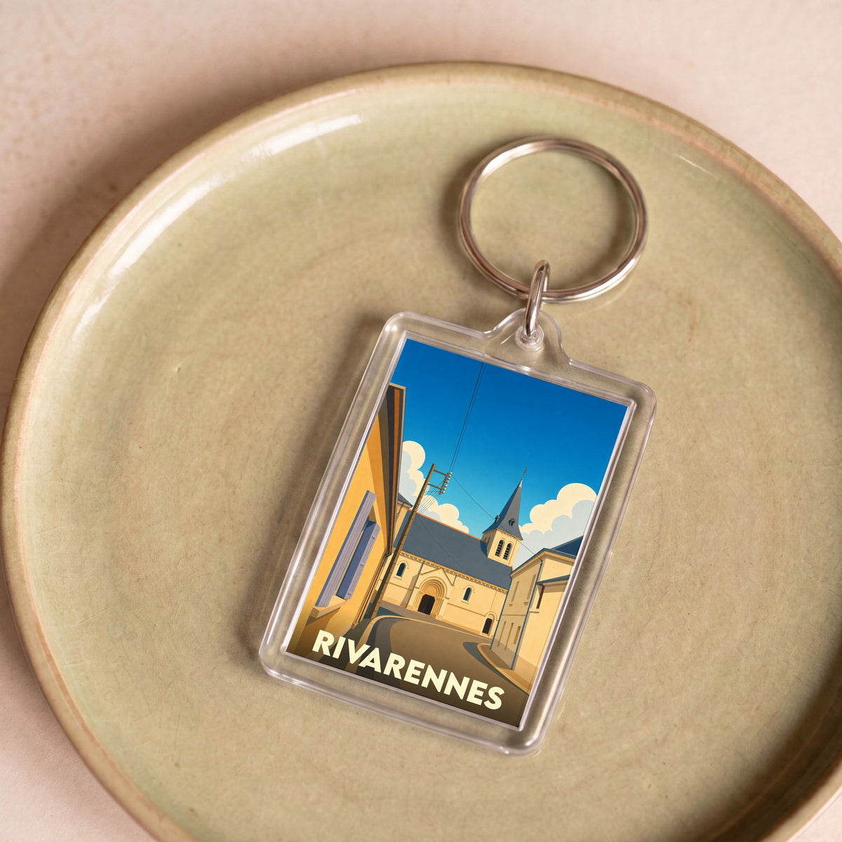 Porte-clés souvenir de la ville de Rivarennes avec une illustration stylisée d'une église et d'une rue ensoleillée.