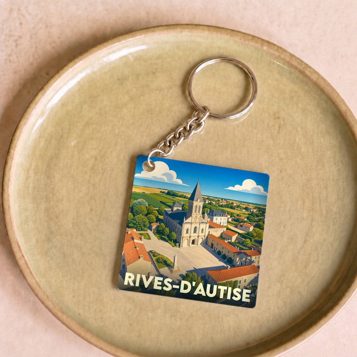 Porte-clés souvenir de la ville de Rives-d'Autise avec une illustration stylisée de son église et de sa place.