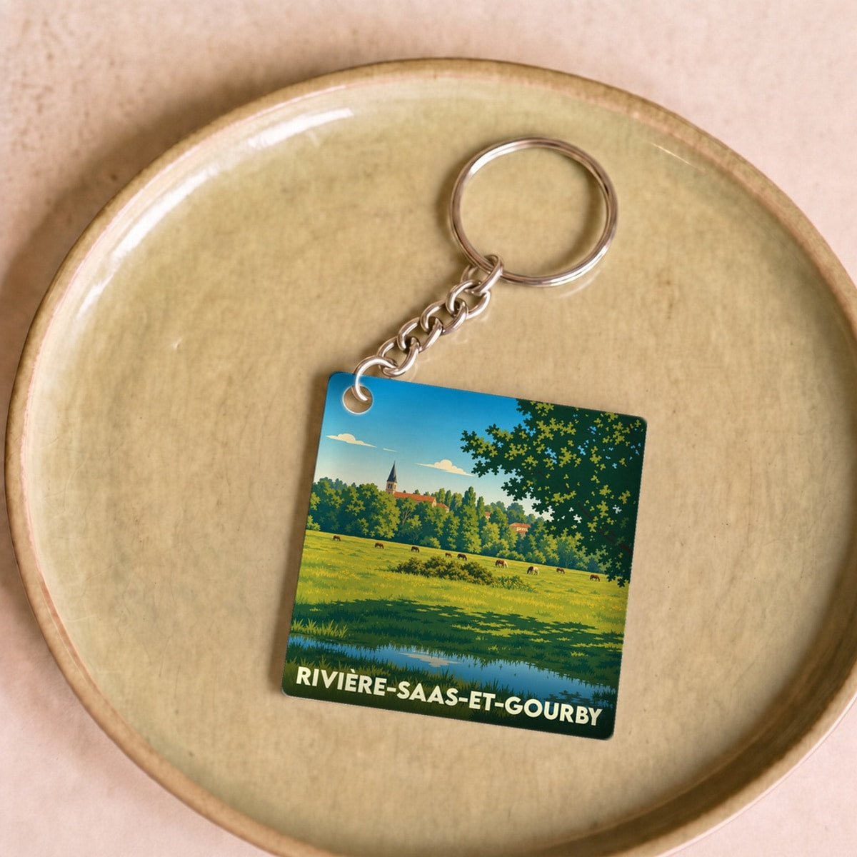 Porte-clés souvenir de la ville de Rivière-Saas-et-Gourby avec une illustration stylisée de son paysage champêtre.