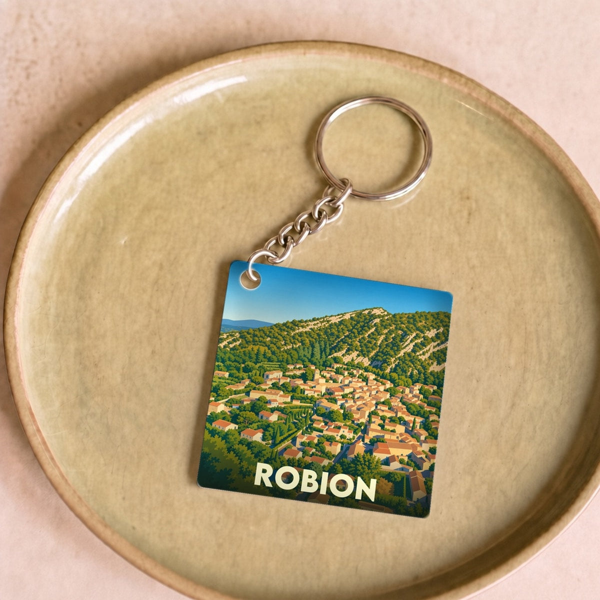 Porte-clés souvenir de la ville de Robion avec une illustration stylisée d'un village provençal.