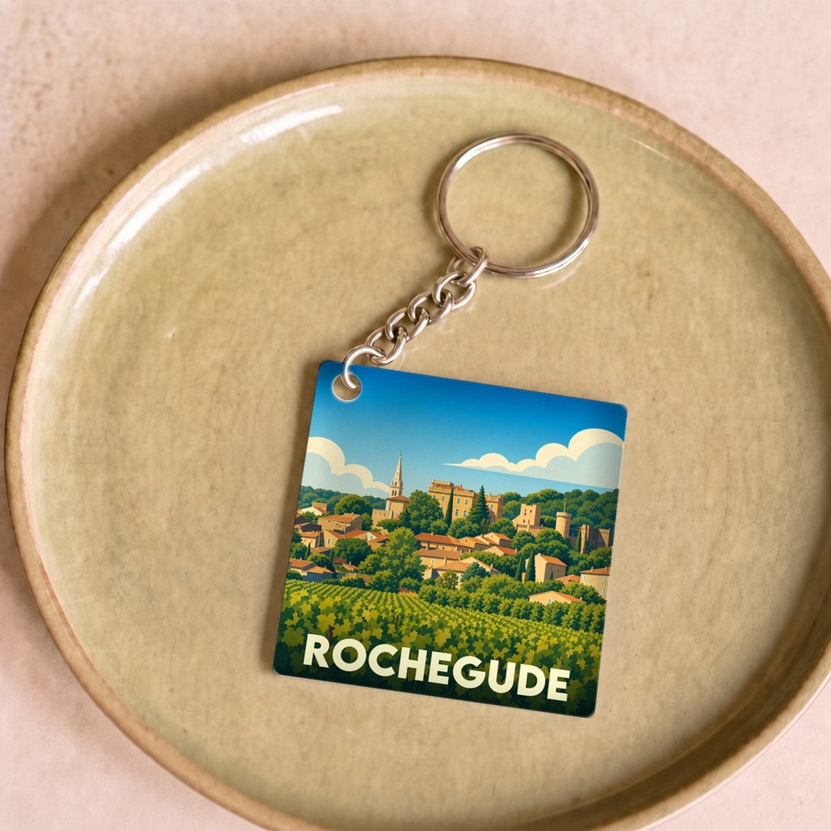 Porte-clés souvenir de la ville de Rochegude avec une illustration stylisée d'un village provençal et de ses vignobles.
