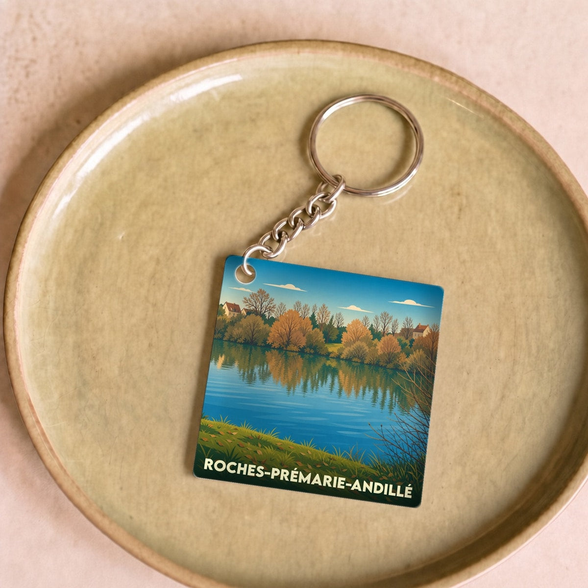 Porte-clés souvenir de la ville de Roches-Prémarie-Andillé avec une illustration stylisée de bord d'eau en automne.