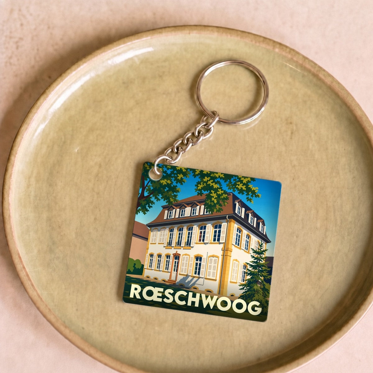 Porte-clés souvenir de la ville de Rœschwoog avec une illustration stylisée d'une maison alsacienne.
