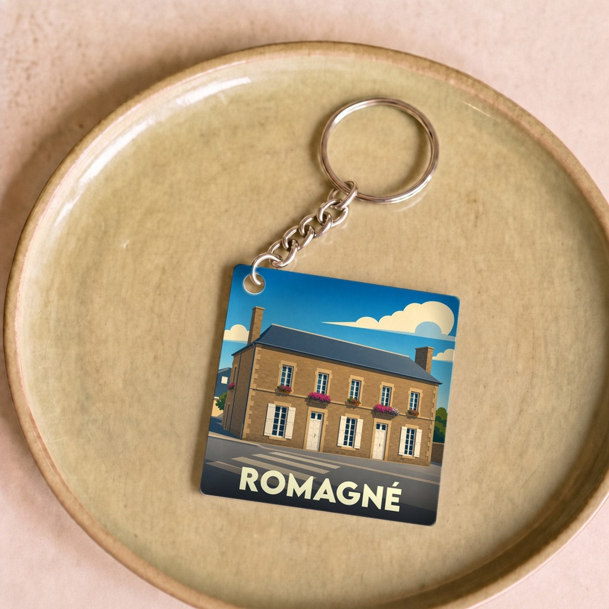 Porte-clés souvenir de la ville de Romagné avec une illustration stylisée d'un bâtiment traditionnel.