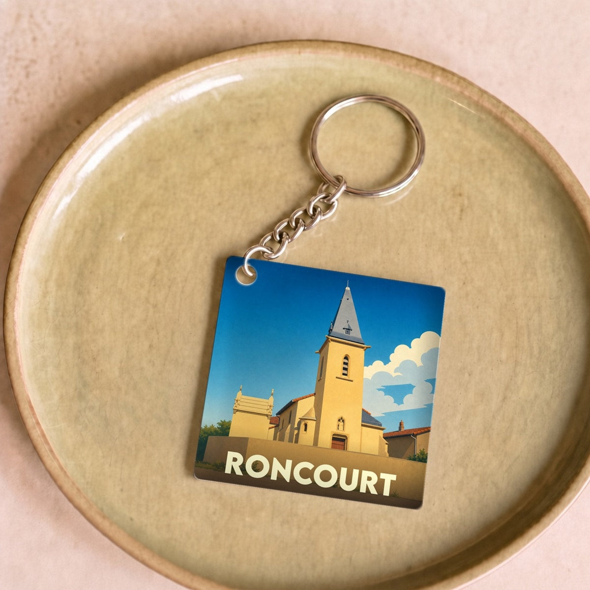 Porte-clés souvenir de la ville de Roncourt avec une illustration stylisée d'une église sous un ciel bleu.