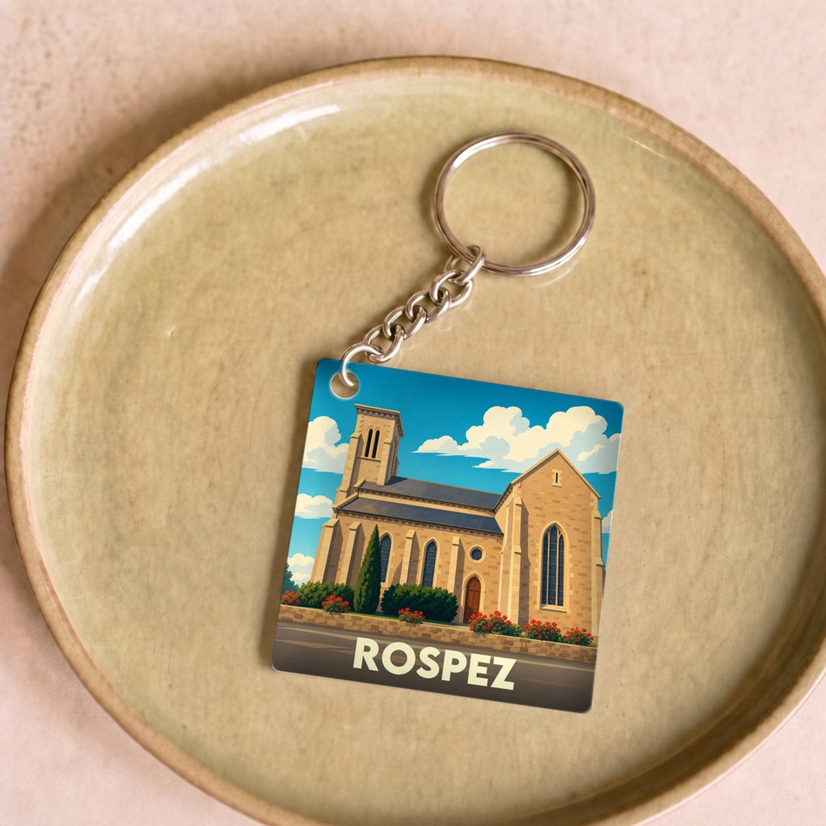 Porte-clés souvenir de la ville de Rospez avec une illustration stylisée de son église sous un ciel bleu.