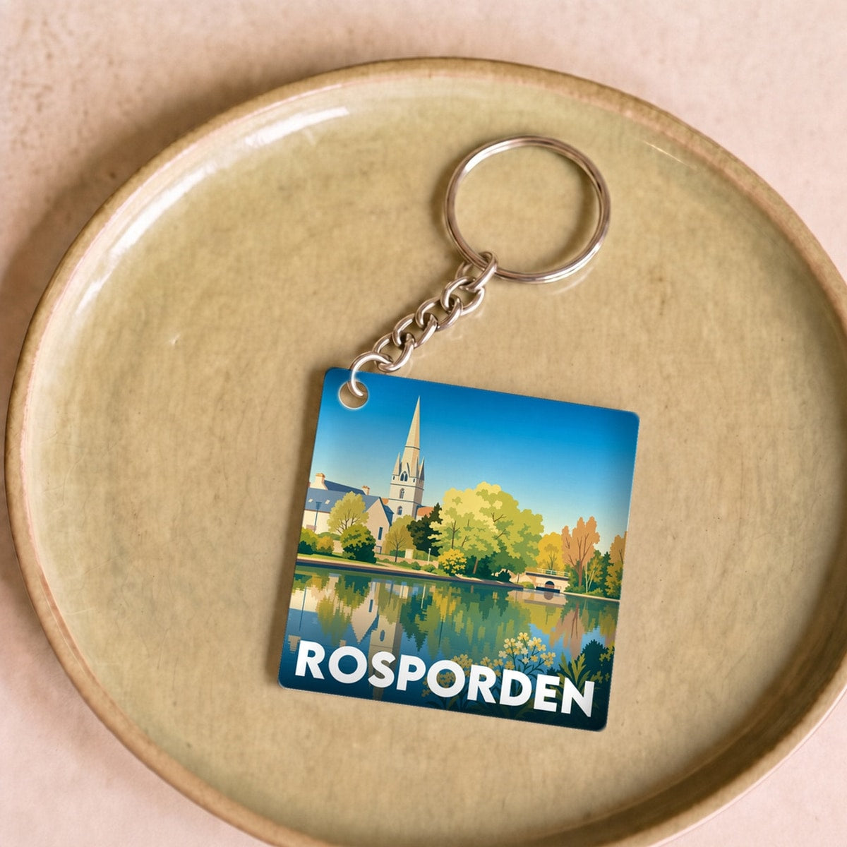 Porte-clés souvenir de la ville de Rosporden avec une illustration stylisée d'un paysage urbain au bord de l'eau.