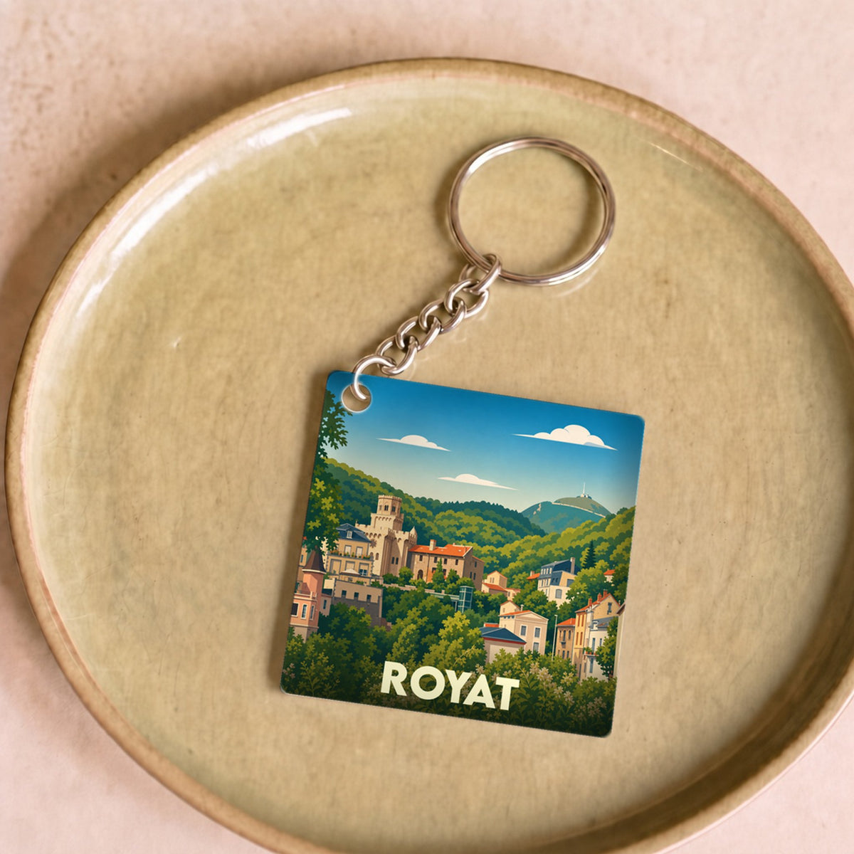 Porte-clés souvenir de la ville de Royat avec une illustration stylisée d'un paysage urbain niché dans la verdure.