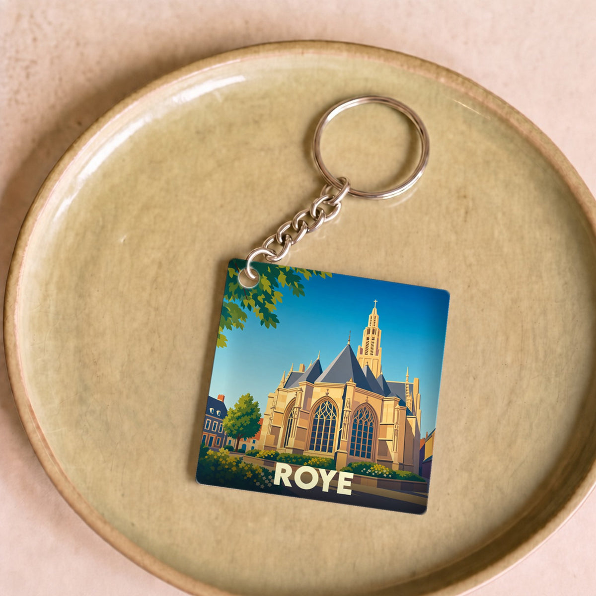 Porte-clés souvenir de la ville de Roye avec une illustration stylisée d'une église sous un ciel bleu.