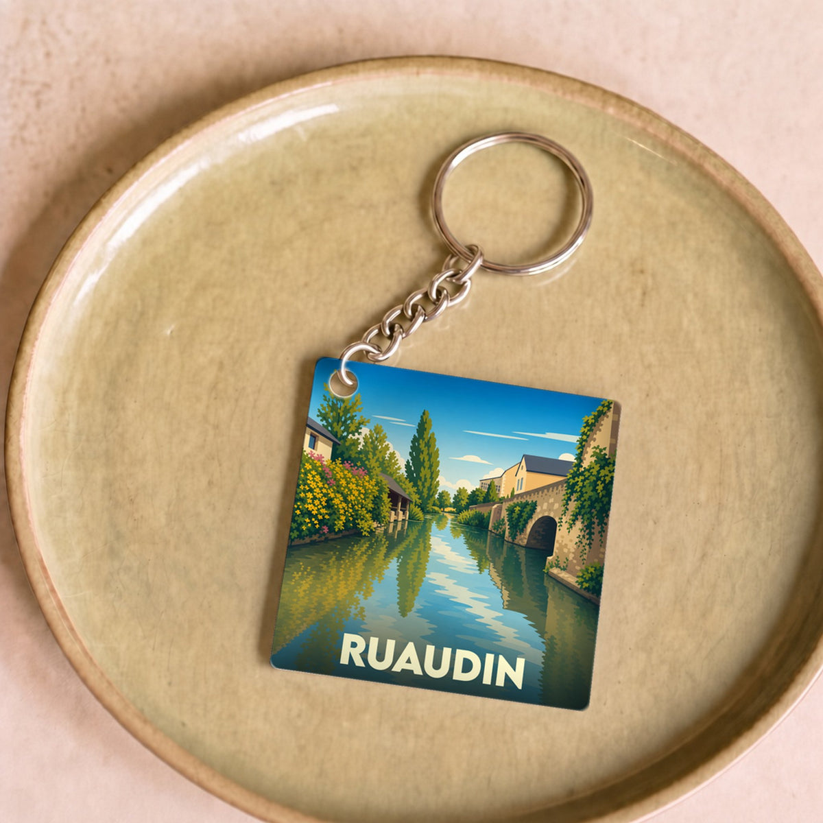 Porte-clés souvenir de la ville de Ruaudin avec une illustration stylisée d'un canal bordé de maisons.