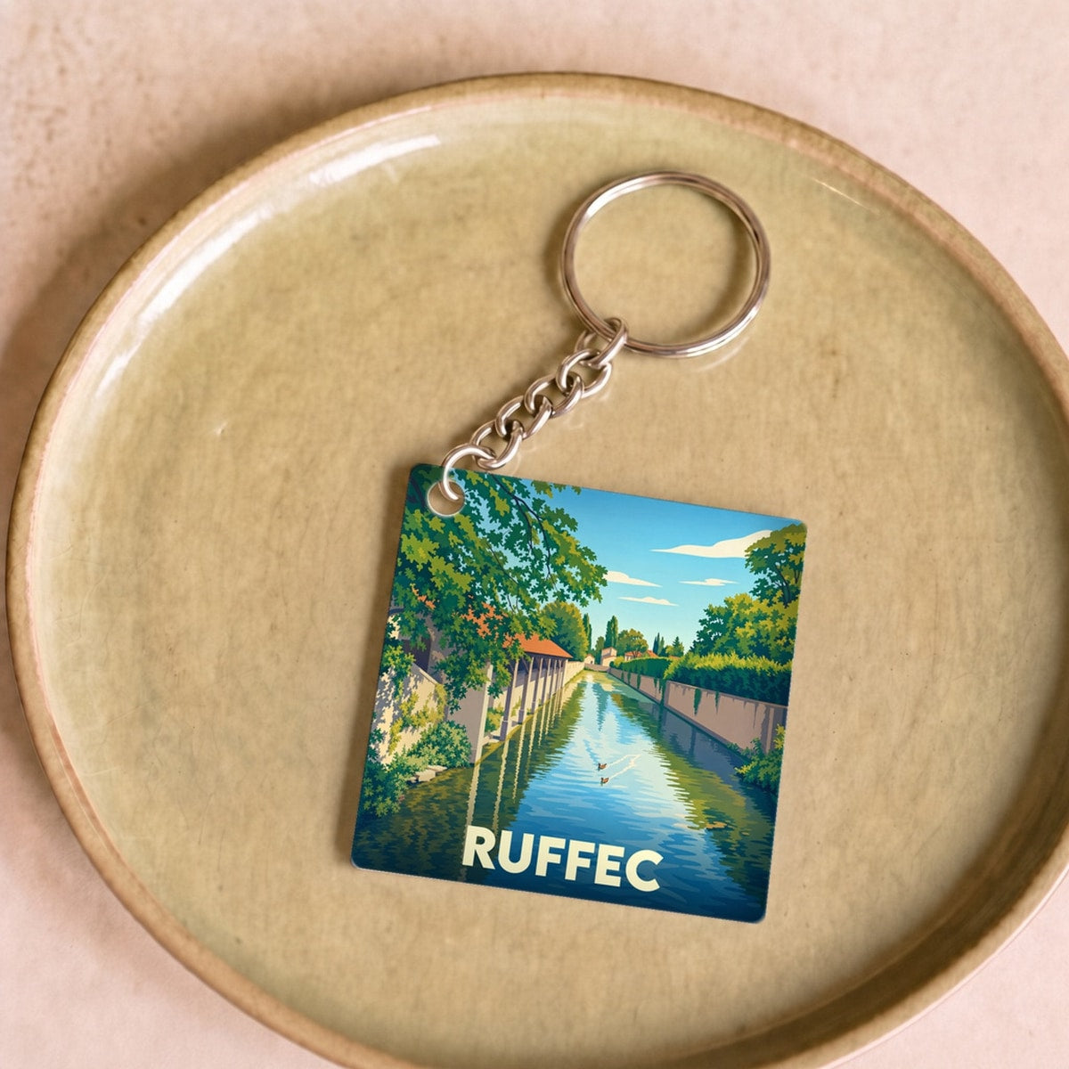 Porte-clés souvenir de la ville de Ruffec avec une illustration stylisée d'un canal bordé de verdure.