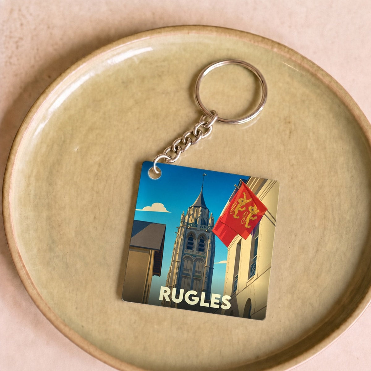 Porte-clés souvenir de la ville de Rugles avec une illustration stylisée de son clocher et du drapeau normand.