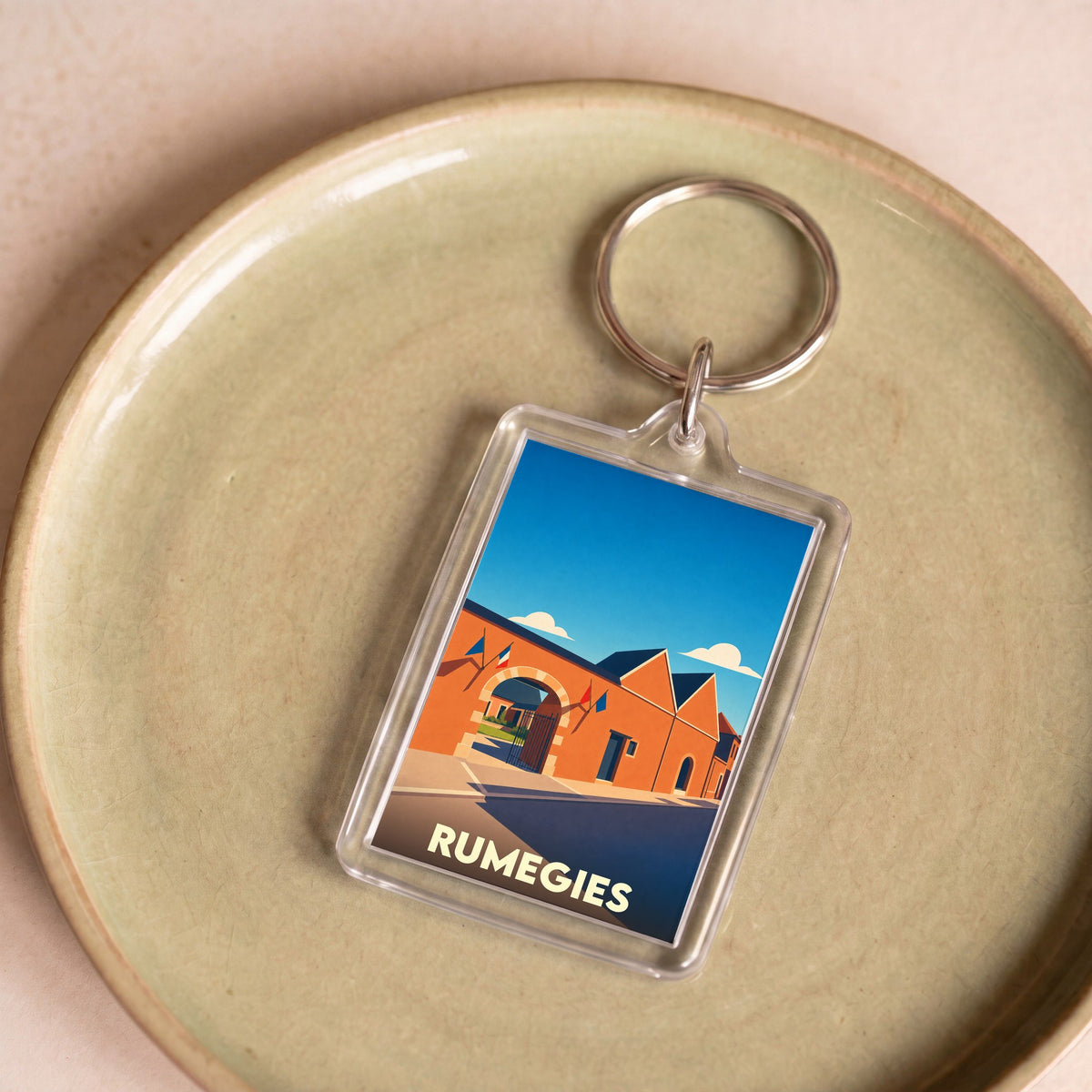 Porte-clés souvenir de la ville de Rumegies avec une illustration stylisée.