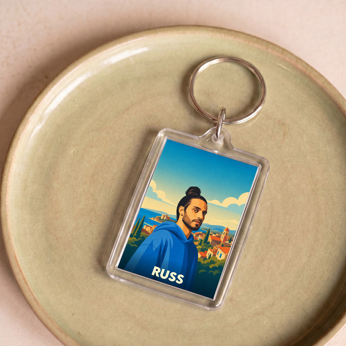 Porte-clés souvenir de la ville de Russ avec une illustration stylisée d'un homme devant un paysage côtier.