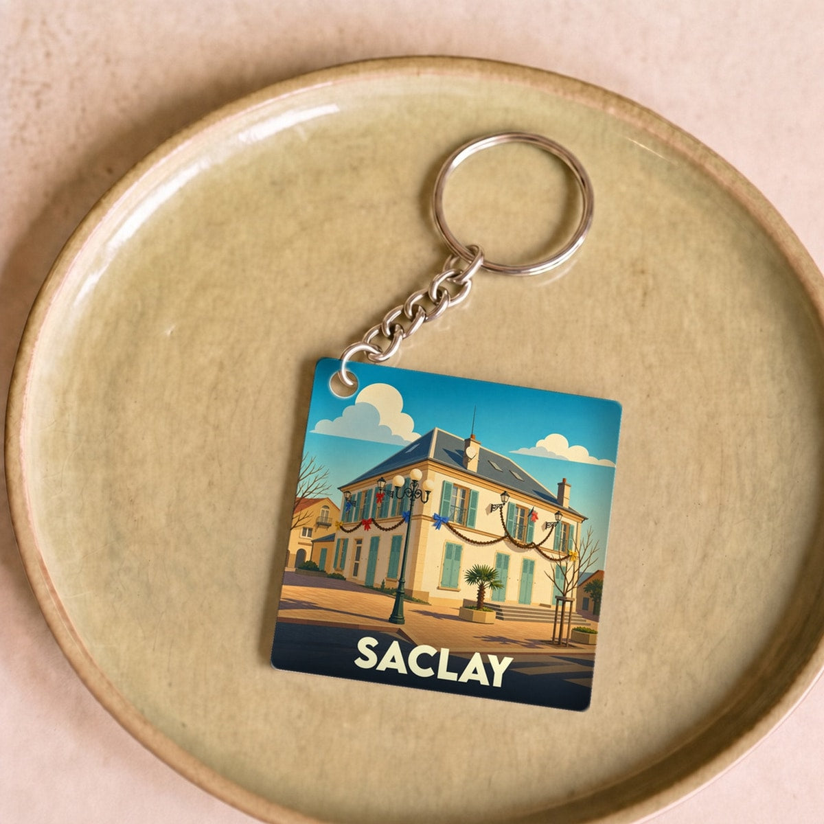 Porte-clés souvenir de la ville de Saclay avec une illustration stylisée d'un bâtiment emblématique.