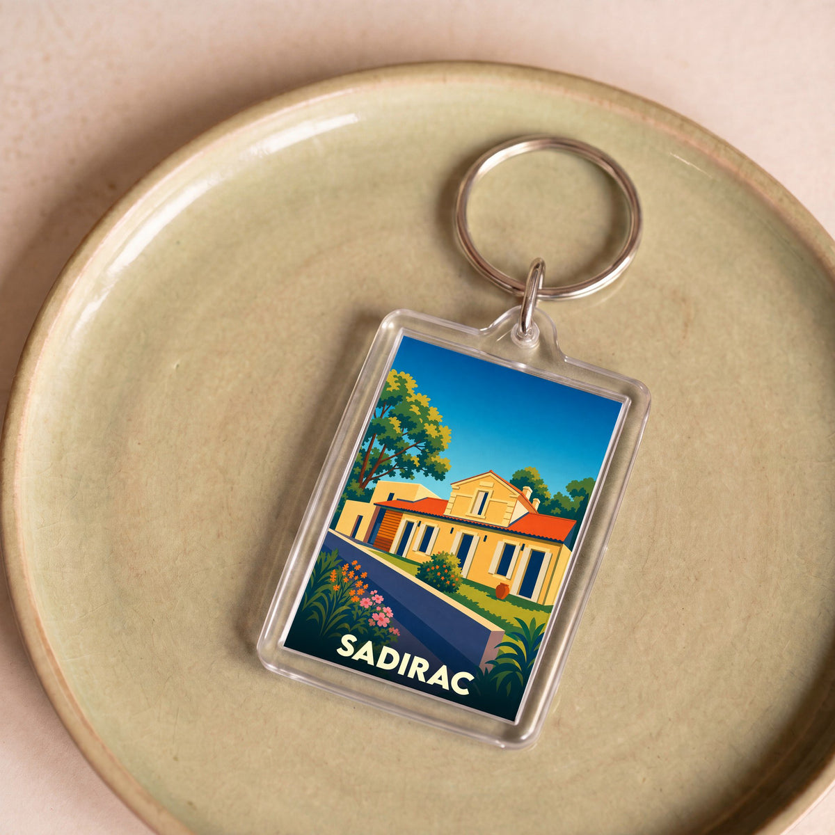 Porte-clés souvenir de la ville de Sadirac avec une illustration stylisée.
