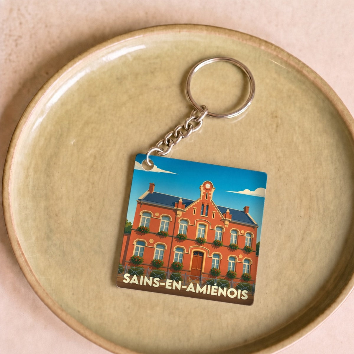 Porte-clés souvenir de la ville de Sains-en-Amiénois avec une illustration stylisée de sa mairie.