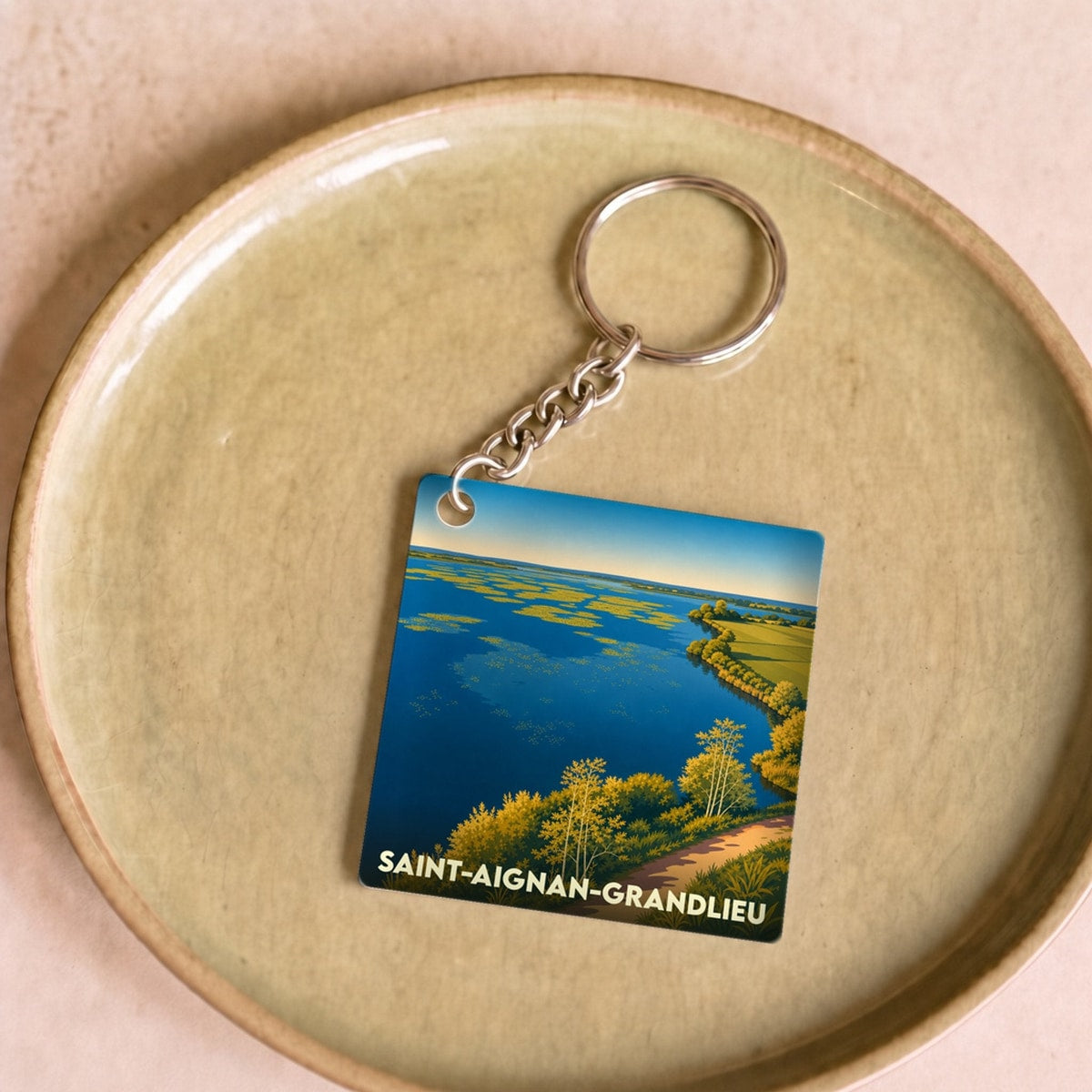 Porte-clés souvenir de la ville de Saint-Aignan-Grandlieu avec une illustration stylisée d'un lac bordé de végétation.