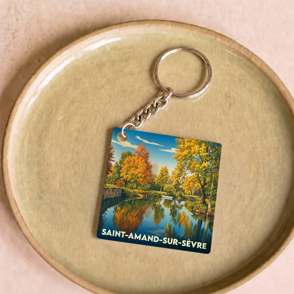 Porte-clés souvenir de la ville de Saint-Amand-sur-Sèvre illustré par un paysage d'automne se reflétant dans l'eau.