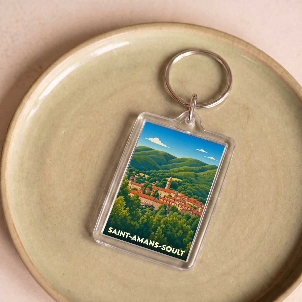 Porte-clés souvenir de la ville de Saint-Amans-Soult avec une illustration stylisée de son paysage vallonné.