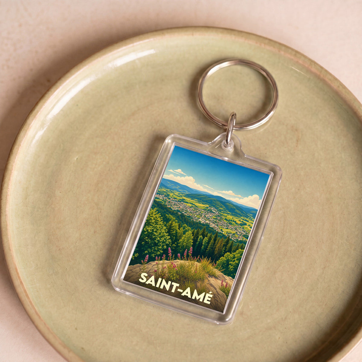 Porte-clés souvenir de la ville de Saint-Amé illustrant un paysage de vallée verdoyante.