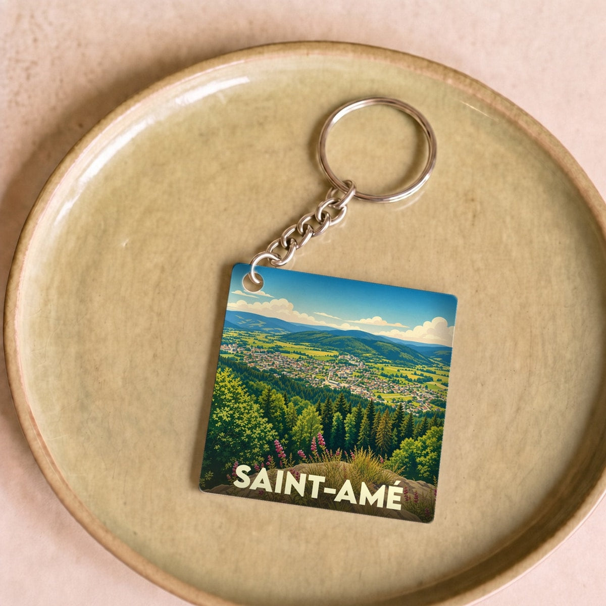 Porte-clés souvenir de la ville de Saint-Amé illustrant un paysage de vallée verdoyante.