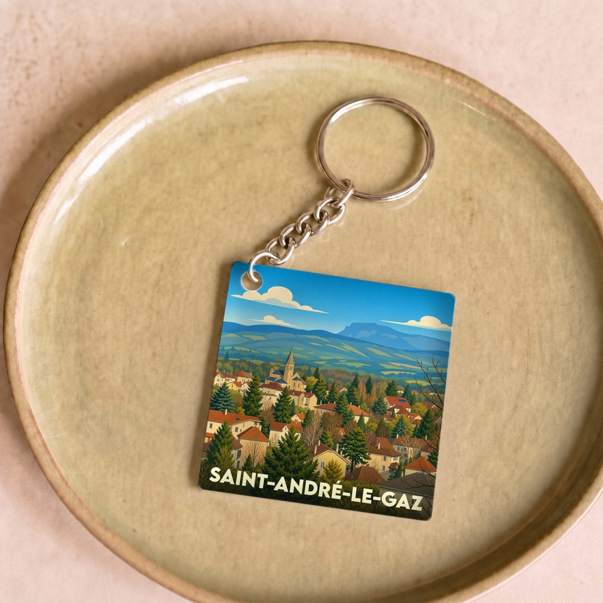 Porte-clés souvenir de la ville de Saint-André-le-Gaz avec une illustration stylisée de son paysage urbain et montagneux.