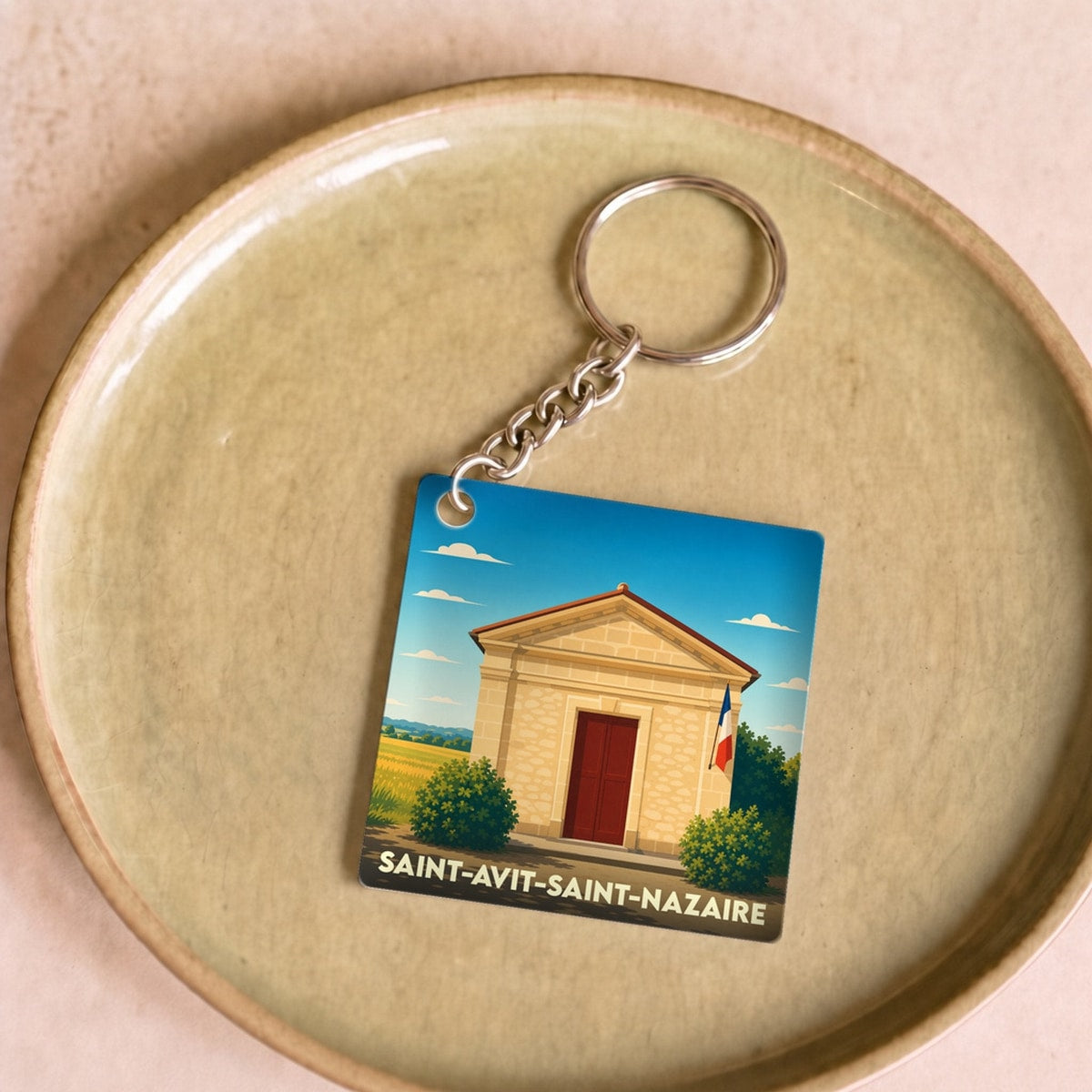 Porte-clés souvenir de la commune de Saint-Avit-Saint-Nazaire avec une illustration stylisée d'un bâtiment local sous un ciel bleu.