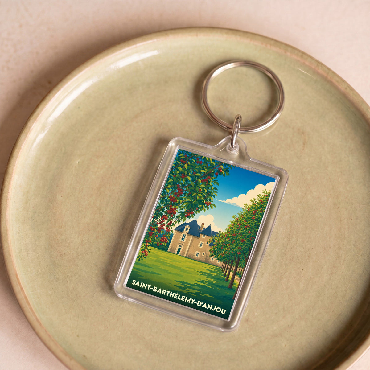 Porte-clés souvenir de la ville de Saint-Barthélemy-d'Anjou avec une illustration stylisée d'un château entouré d'arbres fruitiers.