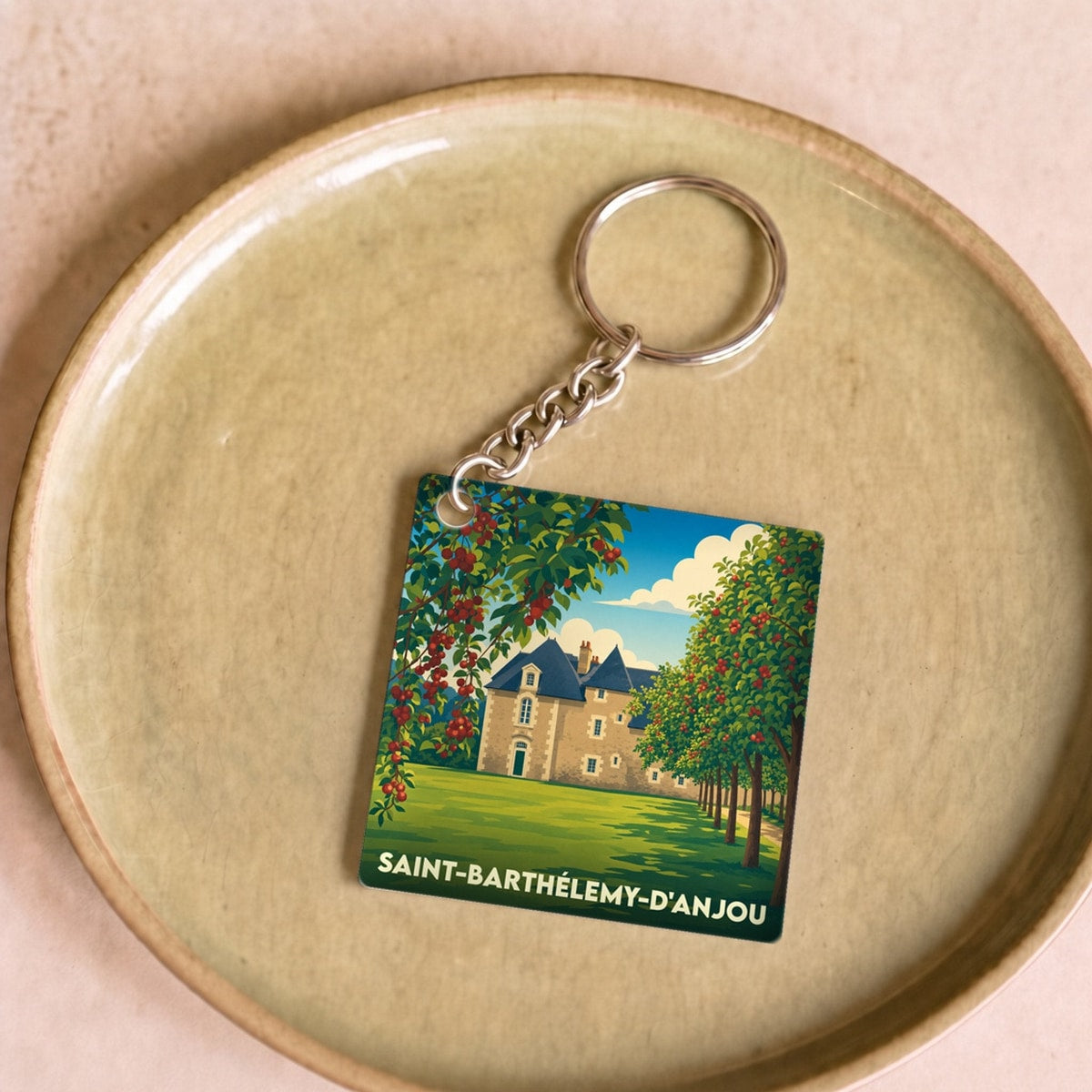 Porte-clés souvenir de la ville de Saint-Barthélemy-d'Anjou avec une illustration stylisée d'un château entouré d'arbres fruitiers.
