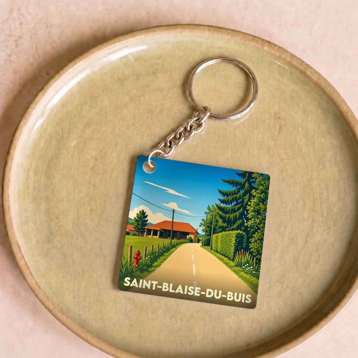 Porte-clés souvenir de la ville de Saint-Blaise-du-Buis avec une illustration stylisée d'un paysage rural.