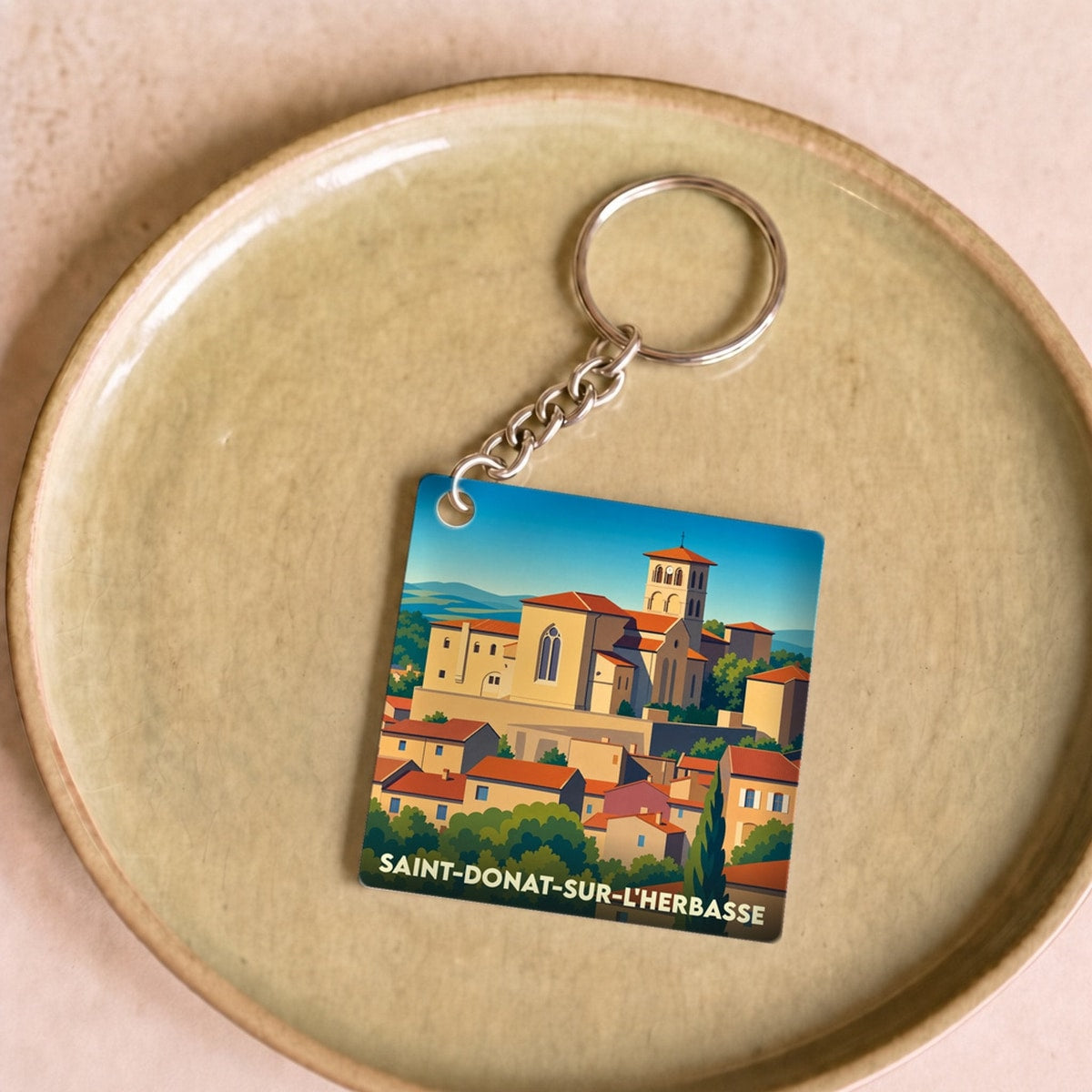 Porte-clés souvenir de la ville de Saint-Donat-sur-l'Herbasse avec une illustration stylisée de son église et de ses toits.