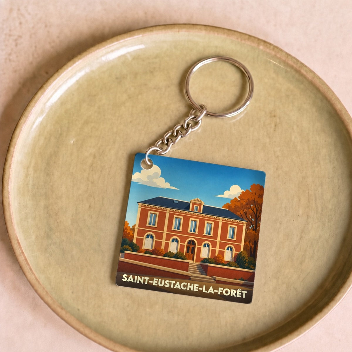 Porte-clés souvenir de la ville de Saint-Eustache-la-Forêt avec une illustration stylisée d'un bâtiment remarquable.